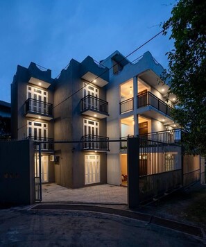 Um edifício residencial com vários andares, varandas, portão fechado e entrada por automóvel.