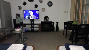 Ein Wohnzimmer mit Fernseher, zwei Massagetischen, einer Couch und Wanddekoration.
