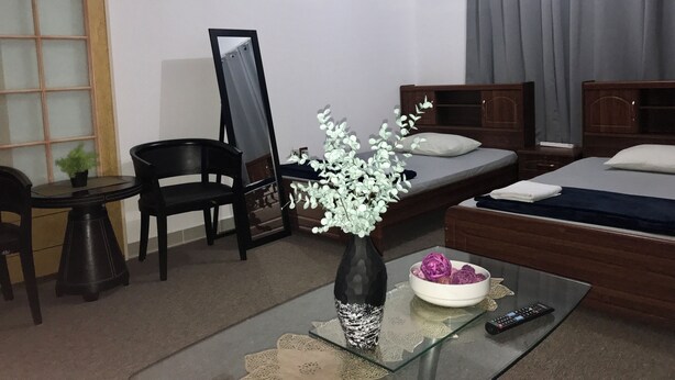 Ein Hotelzimmer mit einem Bett, einem Schreibtisch mit Stuhl, einem Spiegel, einer Vase mit Blumen und einer Fernbedienung auf einem Glastisch.