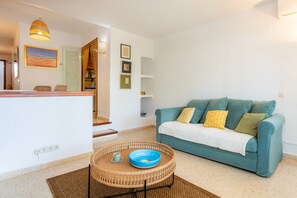 A living room with a teal sofa, a wicker coffee table with a blue bowl, and a hanging light fixture. - Holiday Apartment "Ferrera Suite" with Shared Pool, Private Terrace & Wi-Fi (Cala Ferrera)