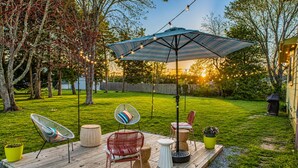 A wooden deck with outdoor furniture, a hanging umbrella, and string lights. - Renovated Coastal Retreat • Walk to Town • Near Stone Harbor & Other Beaches (Cape May Court House)