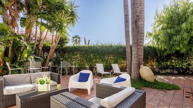 Un patio al aire libre con mobiliario de mimbre, una mesa con una planta y una gran piedra decorativa.