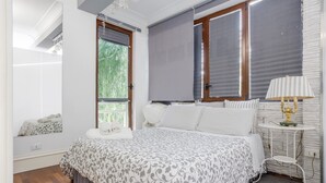 Un dormitorio con cama, ventana, lámpara y estante en la pared.
