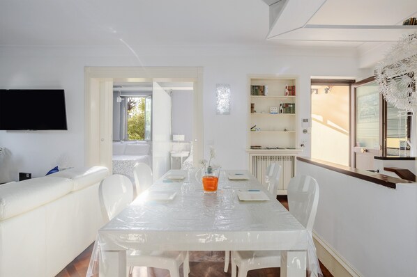 A white dining area with a table, chairs, a TV, and a bookshelf.