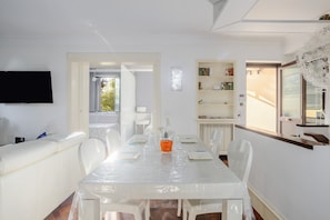 Un comedor blanco con una mesa, sillas, un televisor y una estantería.
