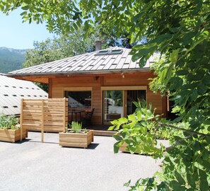 Une cabane en bois avec un toit en pente, une terrasse avec une table et des chaises, et un jardin agrémenté de jardinières en bois.