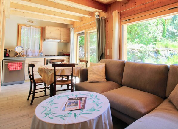 L’intérieur d’un chalet chaleureux comprend un coin repas, une cuisine et un canapé placé près d’une fenêtre.