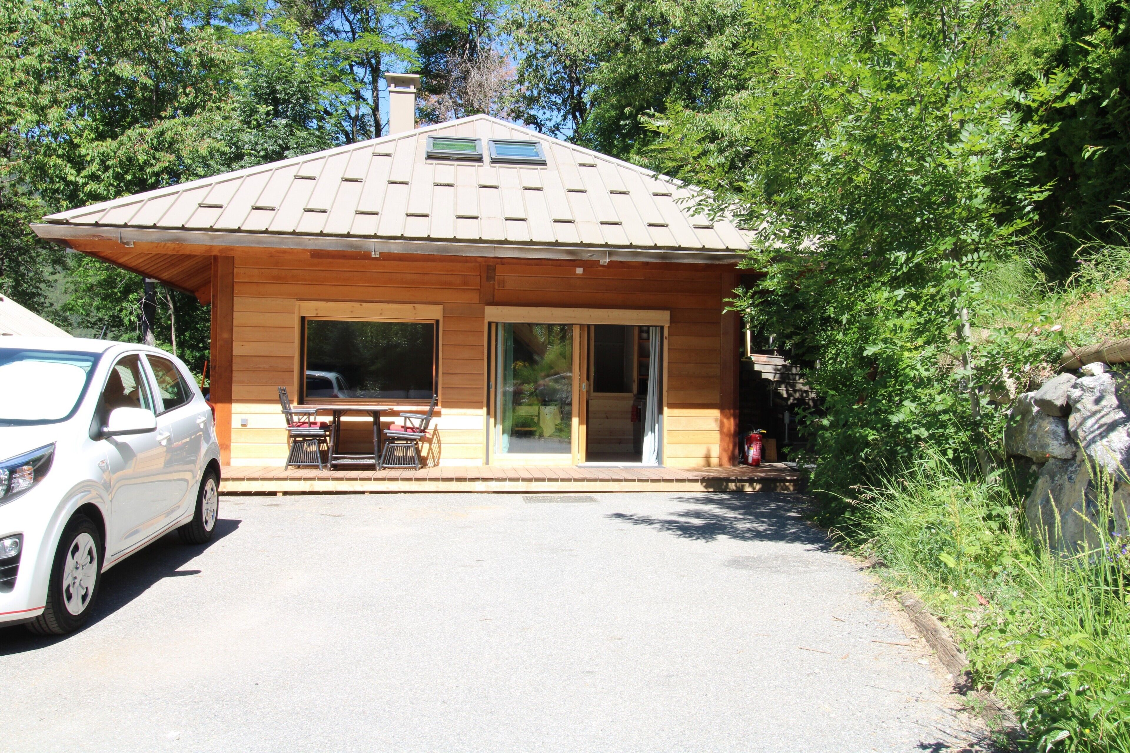 Une cabane en bois avec un toit en tuiles, une véranda et une voiture garée devant.