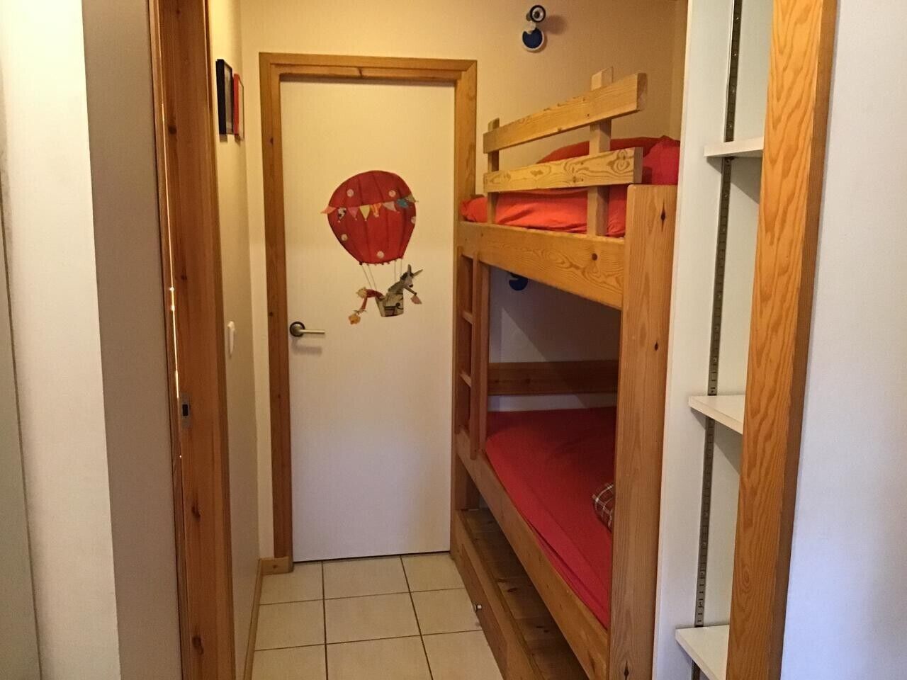 Un couloir étroit avec un lit superposé en bois, une porte blanche et une décoration en forme de ballon rouge.