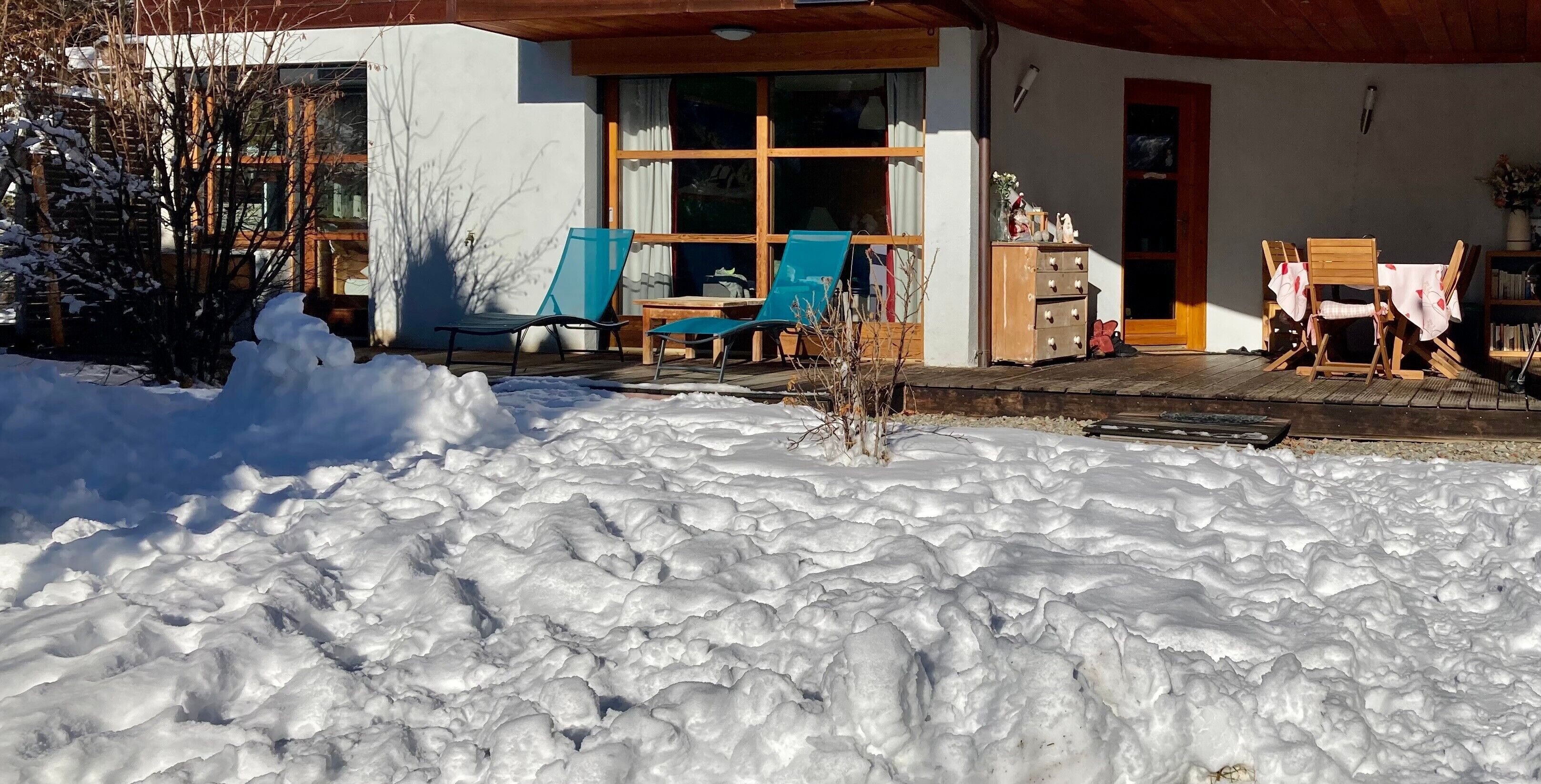 Een besneeuwde buitenruimte met een houten terras, stoelen en een kleine tafel.