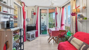Ein gemütliches Zimmer mit einem roten Sofa, einem Esstisch mit einer rot-weißen gepunkteten Tischdecke, einem Fernseher und einem Bücherregal.