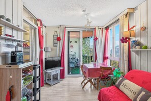 A cozy room with a red sofa, a dining table with a red and white polka dot tablecloth, a TV, and a bookshelf.