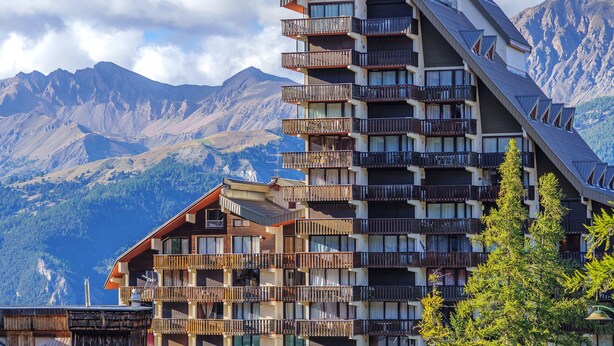 Ein mehrstöckiges Hotel mit Balkonen vor einer Bergkulisse.
