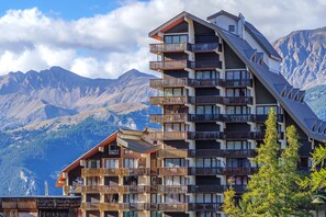 A multi-story hotel with balconies, set against a mountainous backdrop.