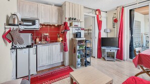 Eine kompakte Küche mit Mikrowelle, Wasserkocher und kleinem Kühlschrank. Es gibt einen Essbereich mit Tisch und Stühlen sowie einen Fernseher auf einem Standfuß.