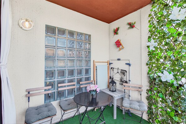 A room with a table, chairs, a decorative wall with a grid of blue-framed windows, and green foliage.