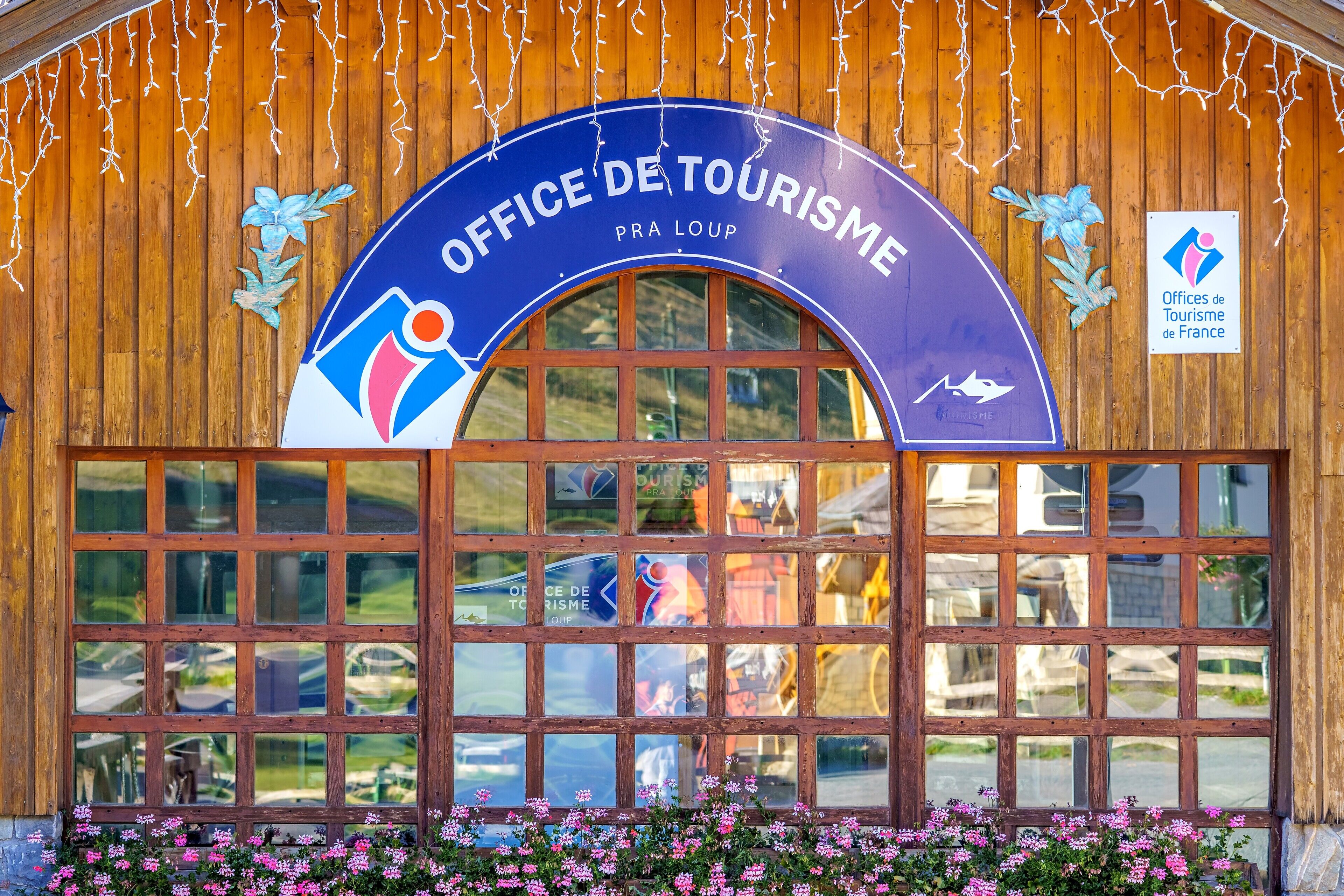 Un bâtiment en bois sur lequel est apposée une grande enseigne indiquant « OFFICE DE TOURISME PRA LOUP » et le logo des Offices de Tourisme de France.