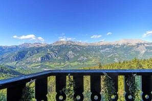 A mountain view from a balcony with a wooden railing and greenery.
