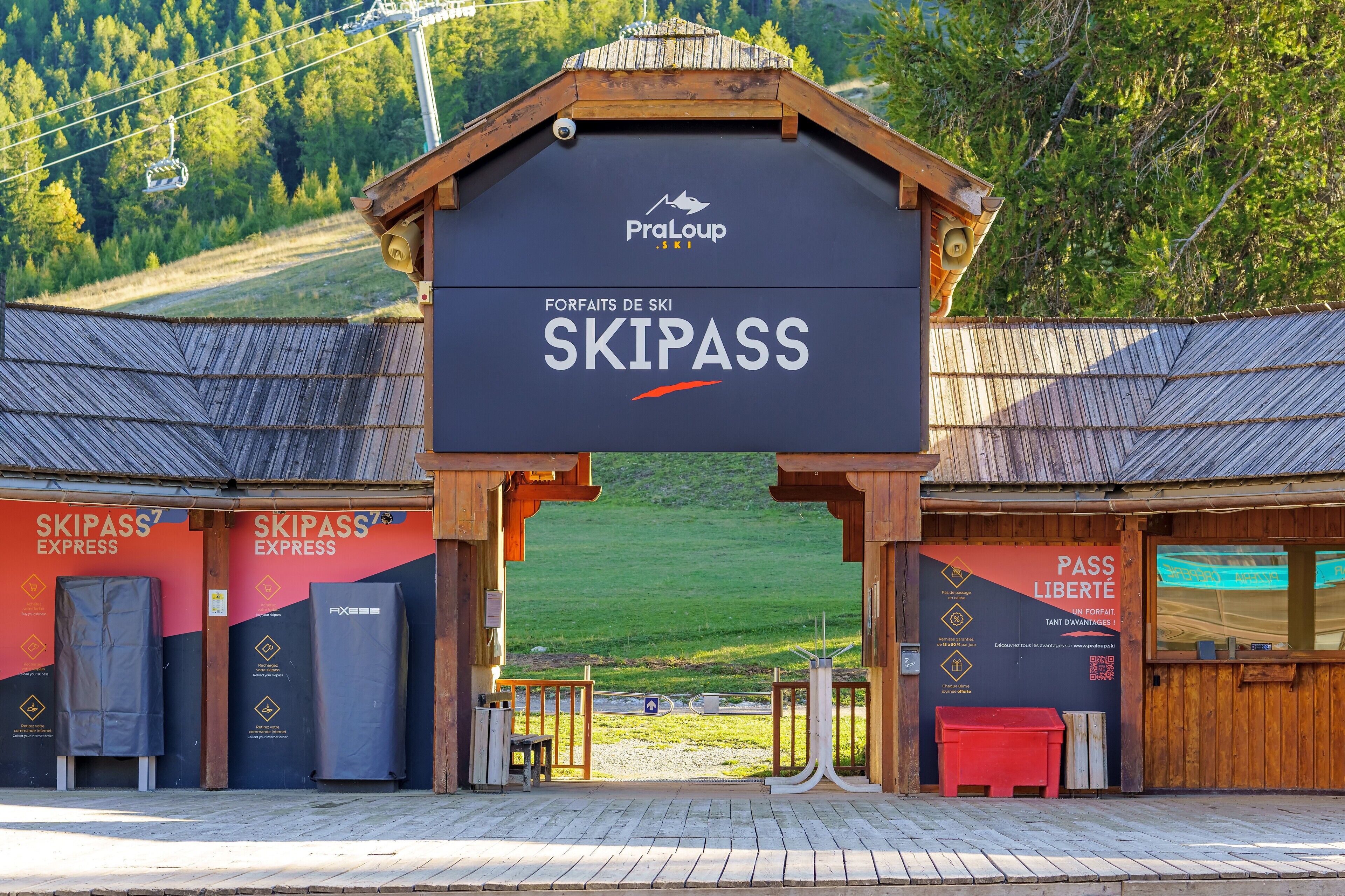 Eine Sesselbahnstation mit Holzbauten, Sesselbahnstühlen und einem Schild mit der Aufschrift 'SKIPASS EXPRESS' und 'SKIPASS'.