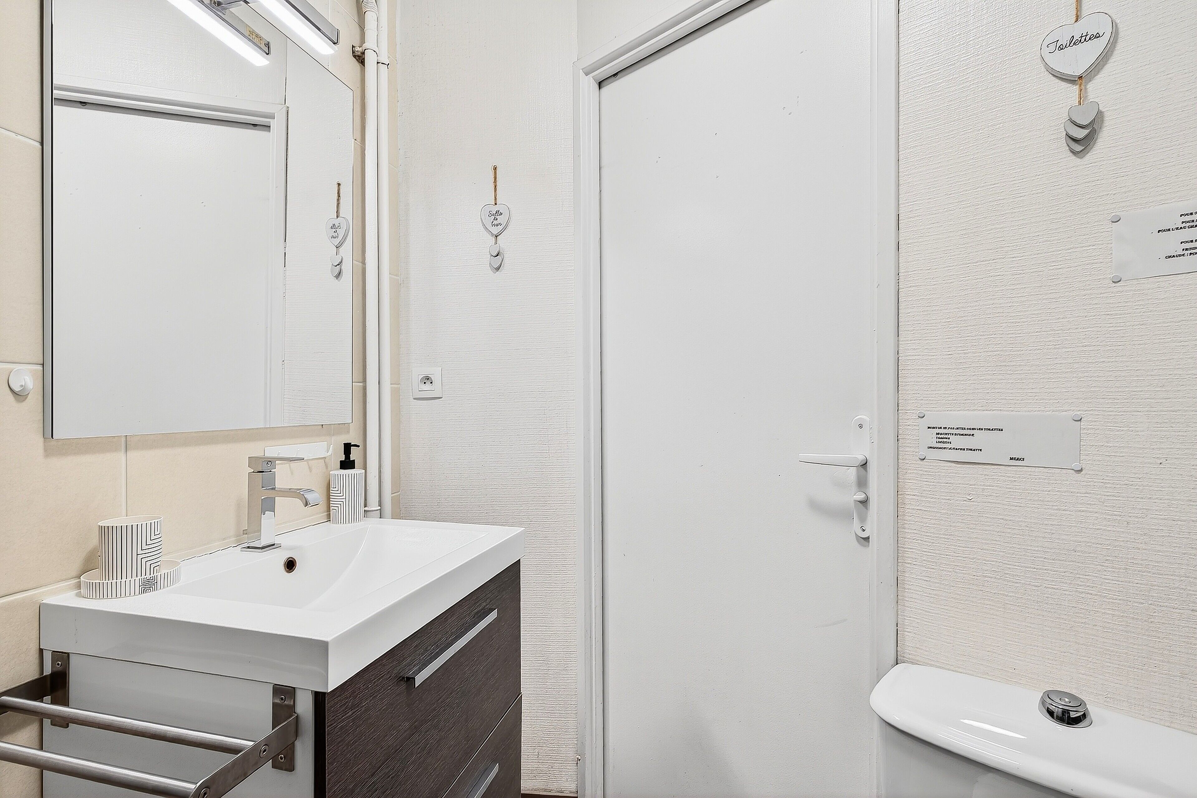 A bathroom with a white sink, mirror, and toilet. There are towels and a soap dispenser on the sink.