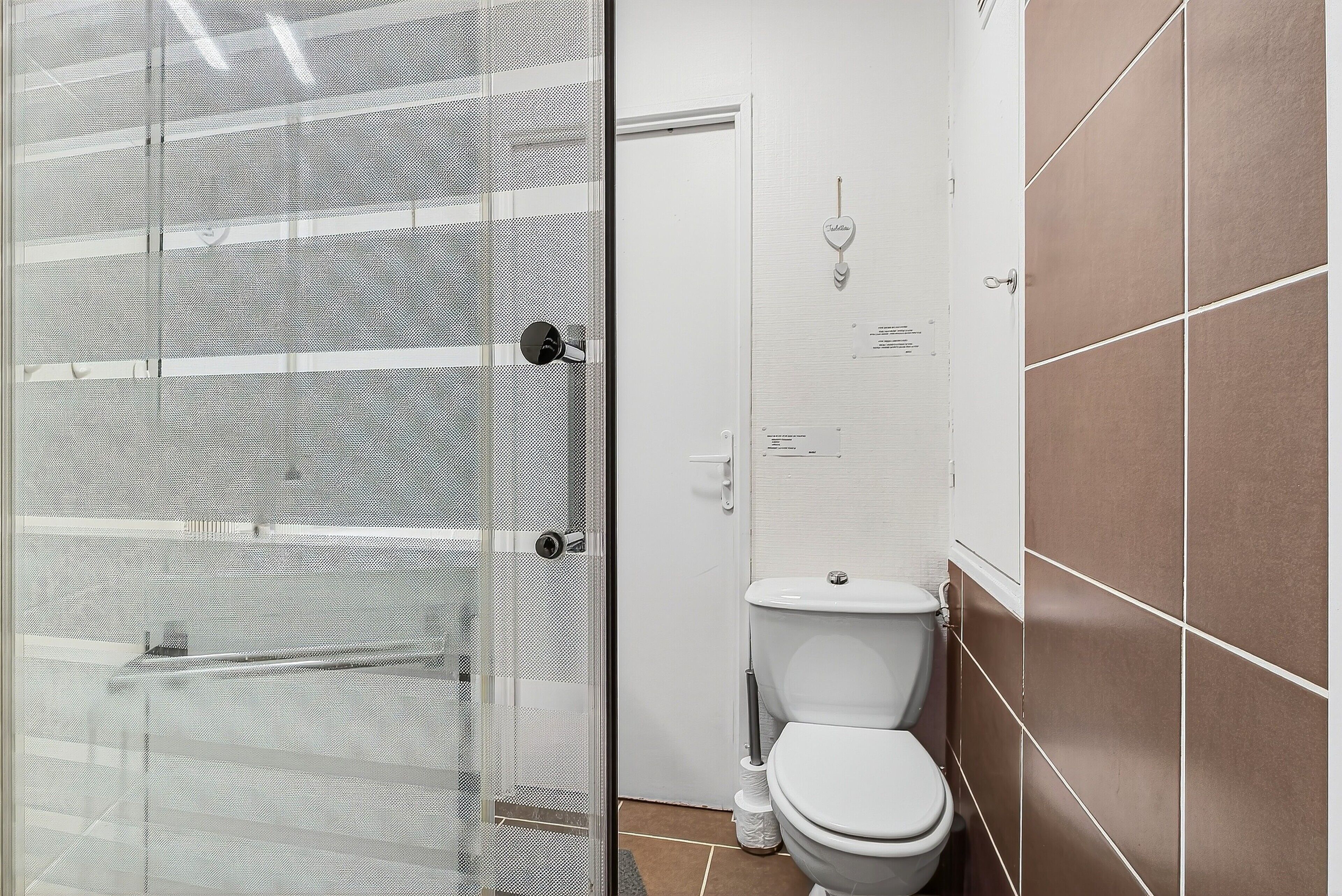 A bathroom with a toilet, a glass shower enclosure, and a tiled wall.
