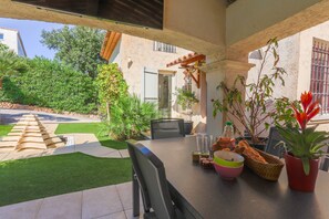 Patio esterno con tavolo apparecchiato per mangiare, circondato da piante in vaso e vista su un giardino.