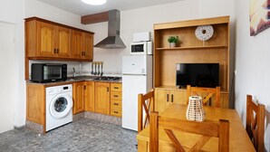 A compact kitchen with wooden cabinets, a washing machine, a microwave, a stove, and a dining area with a table and chairs. - Holiday Home 'Casa Francisco' with Private Pool, Private Terrace and Air Conditioning (Conil de la Frontera)