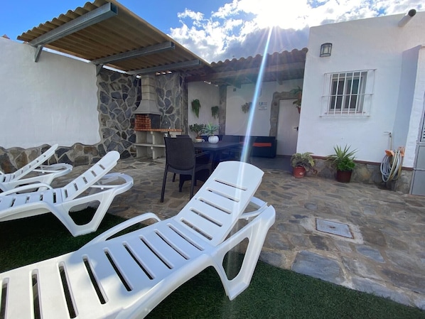 Un patio con sillones de descanso, un muro de piedra, un horno de ladrillo y una zona de estar cubierta.