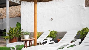 Outdoor lounge chairs, a small table, and potted plants against a white wall. - Holiday Home 'Casa Francisco' with Private Pool, Private Terrace and Air Conditioning (Conil de la Frontera)