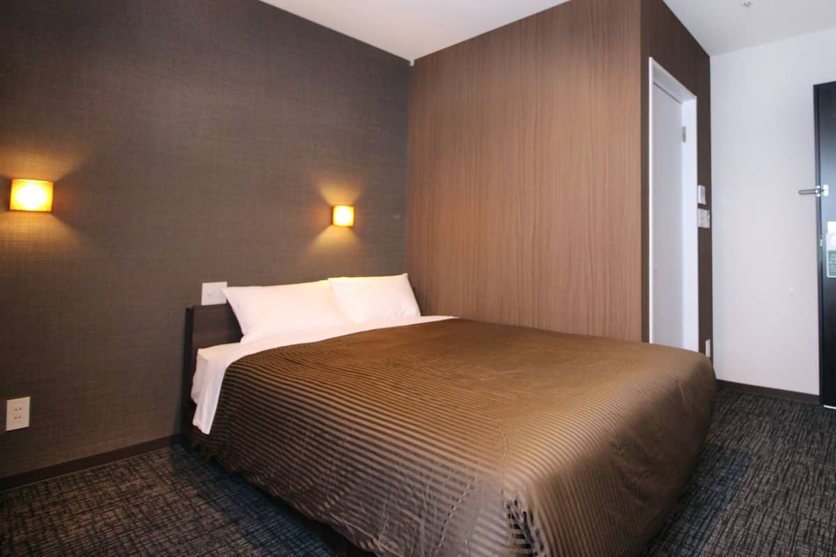 A hotel room with a large bed, two wall-mounted lights, and a door to the right.