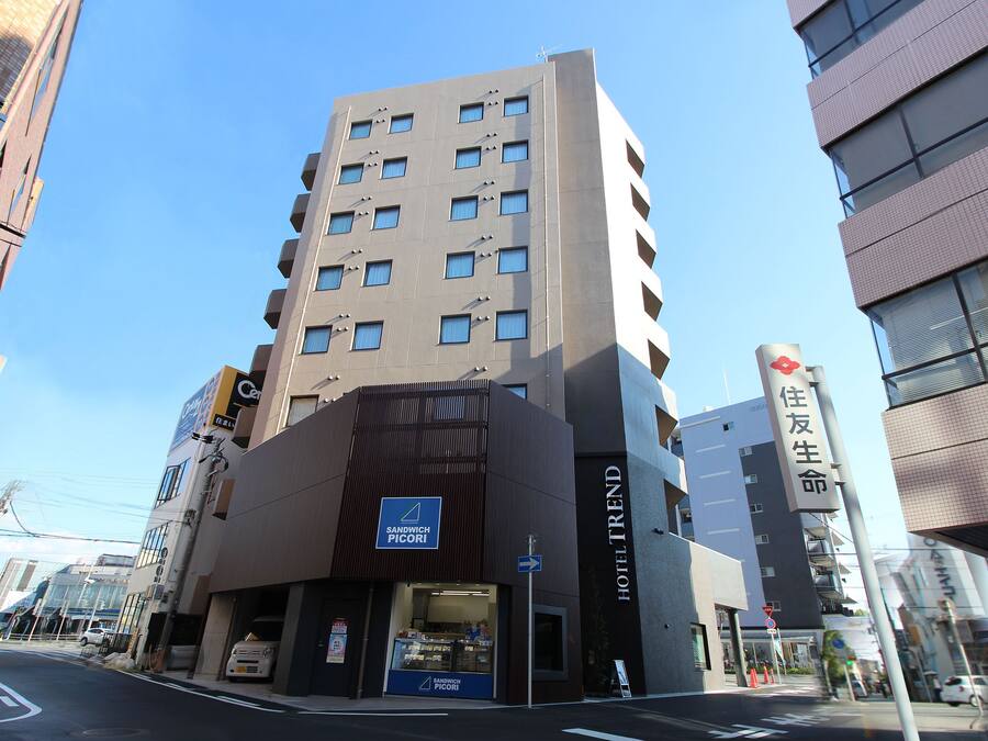 Un hôtel moderne à plusieurs étages, avec un café-sandwich bien visible au rez-de-chaussée et un ciel dégagé.