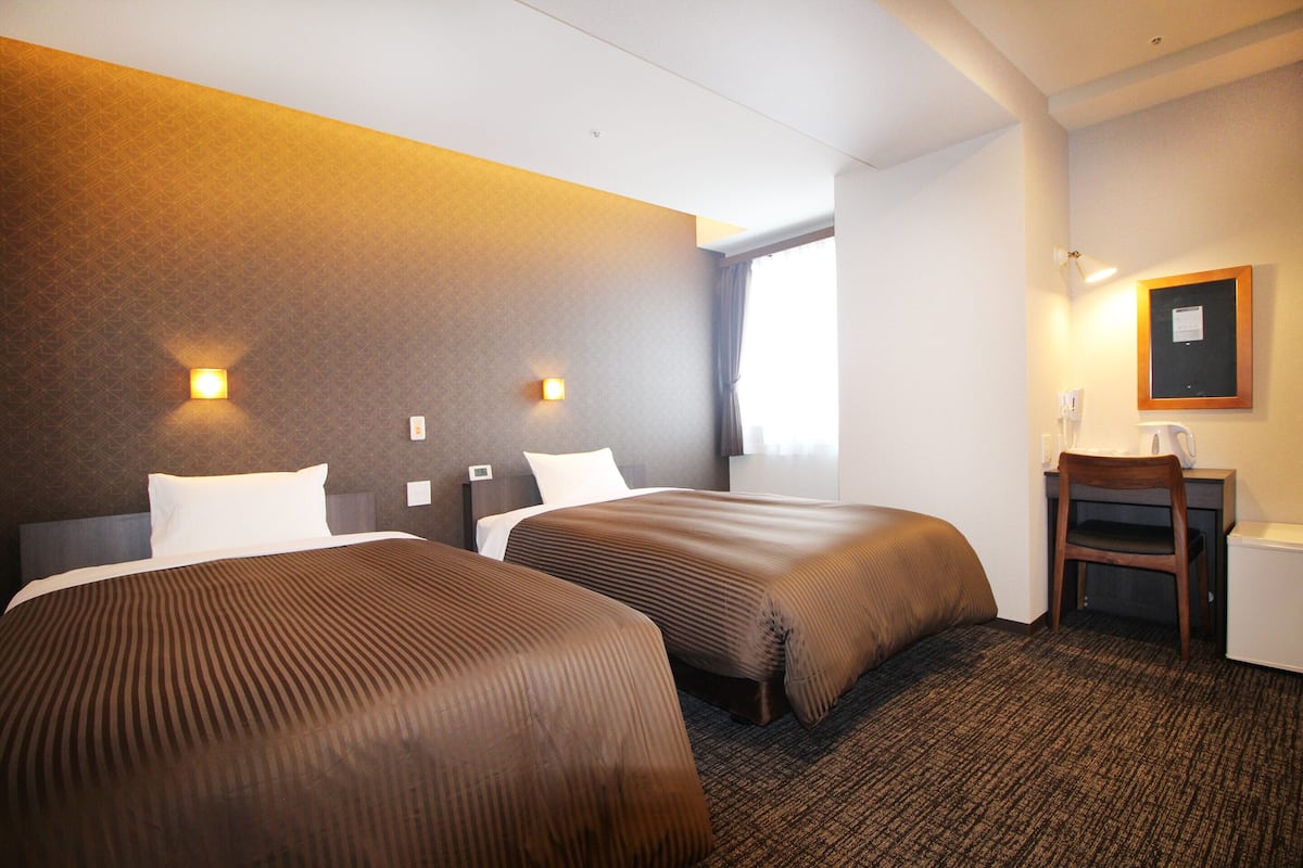 A hotel room with two beds, a desk, and a chair.