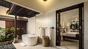A modern bathroom with a freestanding bathtub, a large mirror, and a small trash bin. - Villa Gading by Alfred in Bali (Seminyak)