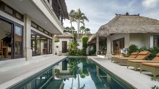 A pool area with lounge chairs, a thatched-roof structure, and a reflection pool. - Villa Gading by Alfred in Bali (Seminyak)