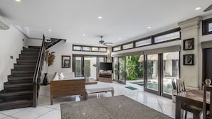 A spacious living area with a staircase, a large TV, and a dining table. - Villa Gading by Alfred in Bali (Seminyak)