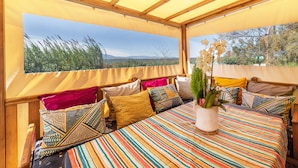 A room with a large bed, multiple pillows, a potted plant, and a view of the outdoors.