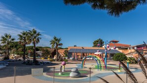 A playground with colorful play structures, palm trees, and a building with a red roof in the background.