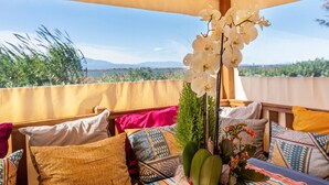 A covered outdoor seating area with a view of the landscape, a table with a vase of flowers, and colorful cushions.