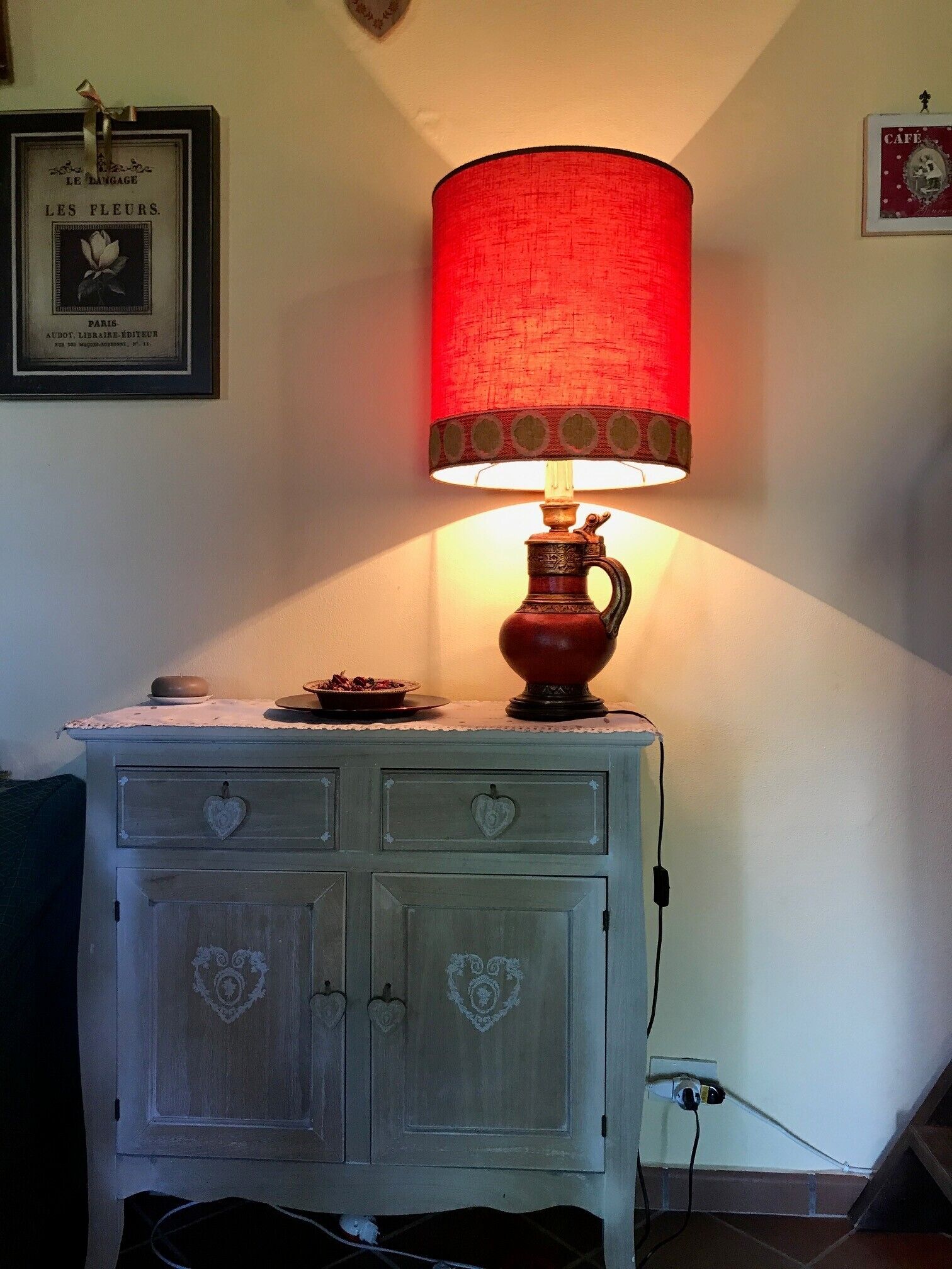 A vintage-style lamp with a red shade on a white cabinet with heart-shaped handles.