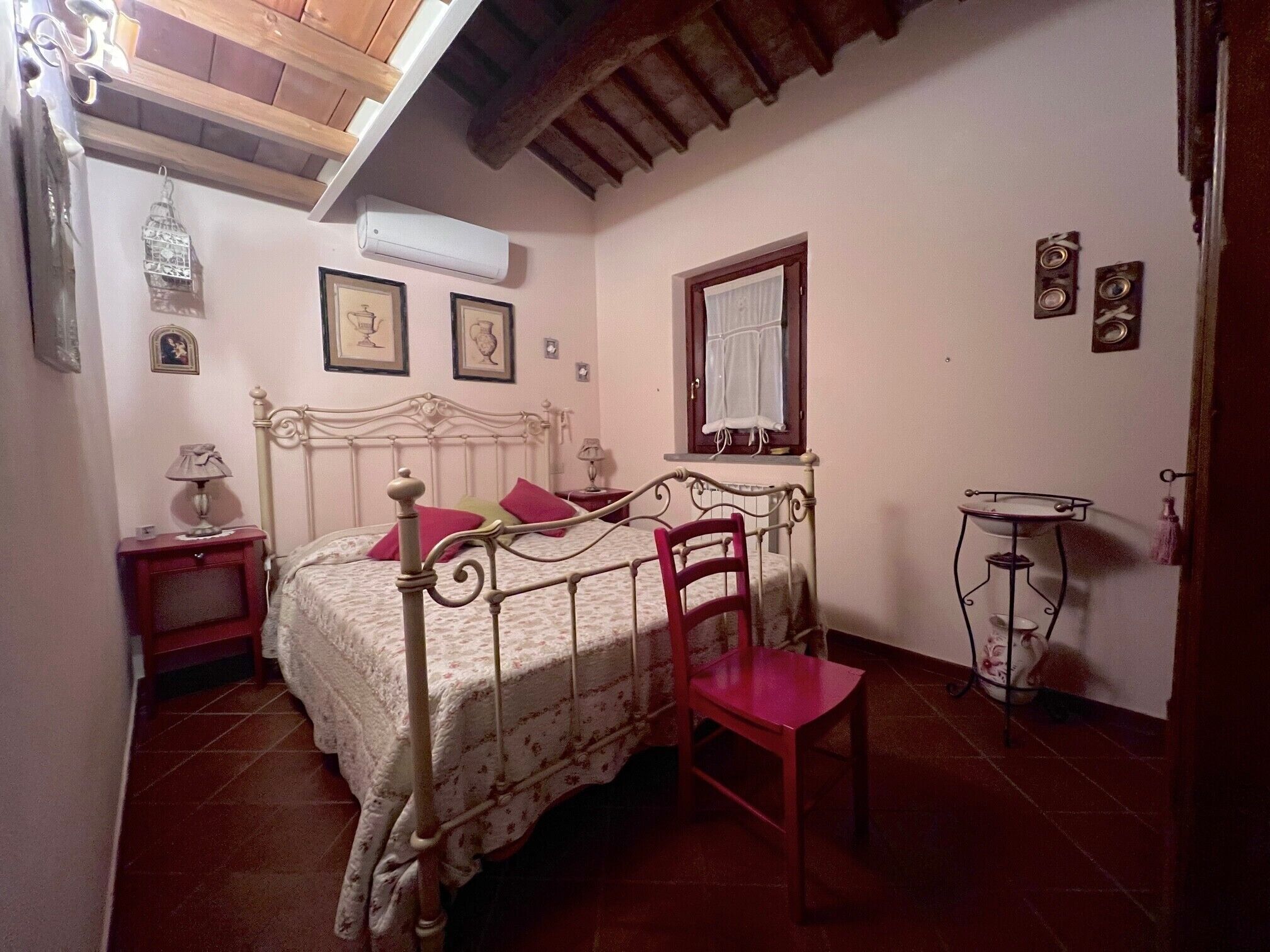 Um quarto com cama, cadeira, mesa de cabeceira, janela e ar condicionado.