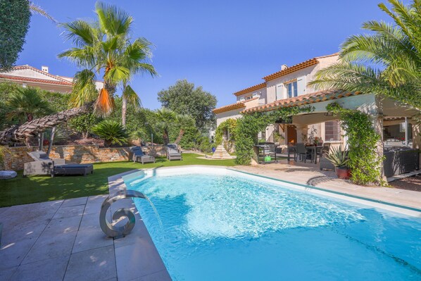 A swimming pool with a sun lounger, palm trees, and a house with a tiled roof. - Villa 'Complète Au Soleil D'Azur' with Sea View, Wi-Fi and Air Conditioning (Fréjus)