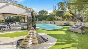 Un patio trasero con piscina, pérgola, mobiliario exterior y un césped bien cuidado.