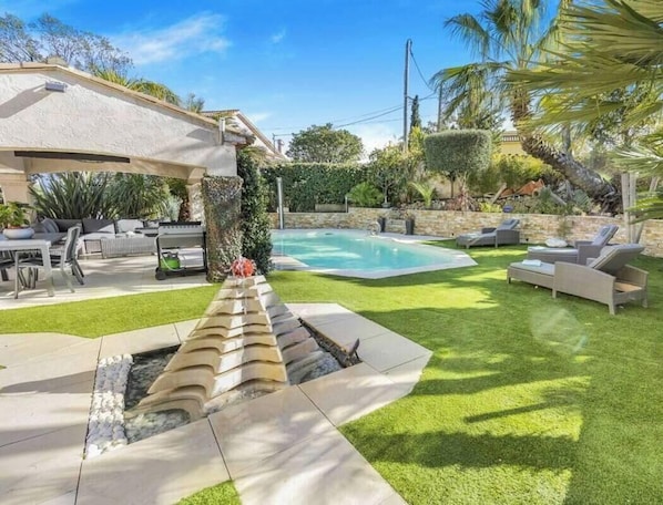 Un jardin avec une piscine, une pergola, du mobilier d’extérieur et une pelouse bien entretenue.