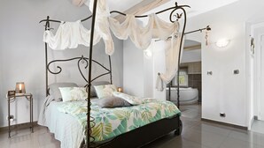 Una cama con dosel y mosquitera, una mesita de noche con lámpara, y vistas a un baño con bañera.