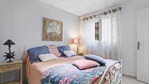 A bedroom with a bed, bedside tables, a lamp, a wall decoration, and a window with curtains.