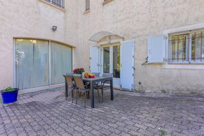 Un patio con una mesa, sillas, una planta en maceta y un edificio con una puerta y una ventana.