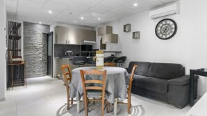 A modern living room with a grey sofa, a dining table with chairs, and a kitchen area in the background.