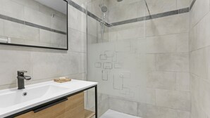 A modern bathroom with a white sink, a mirror, a shower with a glass door, and a tiled wall with a geometric pattern.