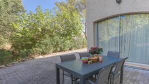 An outdoor patio with a table and chairs, a potted plant, and a window with curtains.
