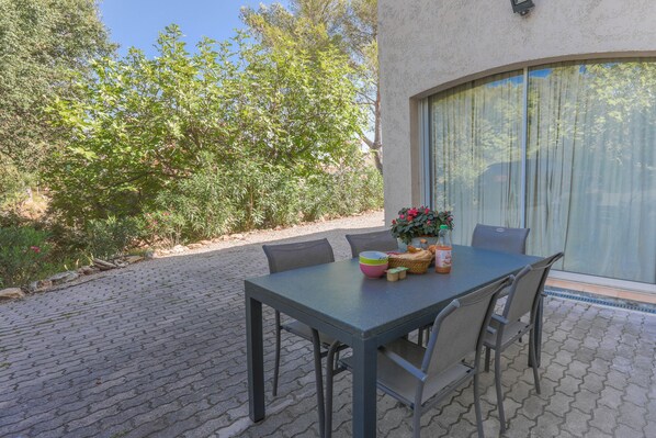 Un patio al aire libre con una mesa y sillas, una planta en maceta y una ventana con cortinas.
